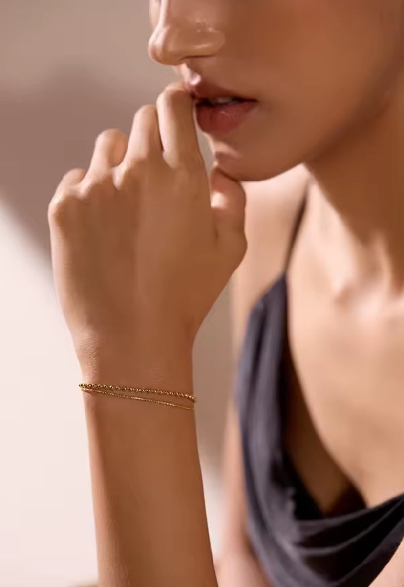 Bracelet Duo Perlé: Double chaîne dorée ornée de perles fines pour un style féminin, chic et tendance, parfait au quotidien ou en occasion spéciale. 